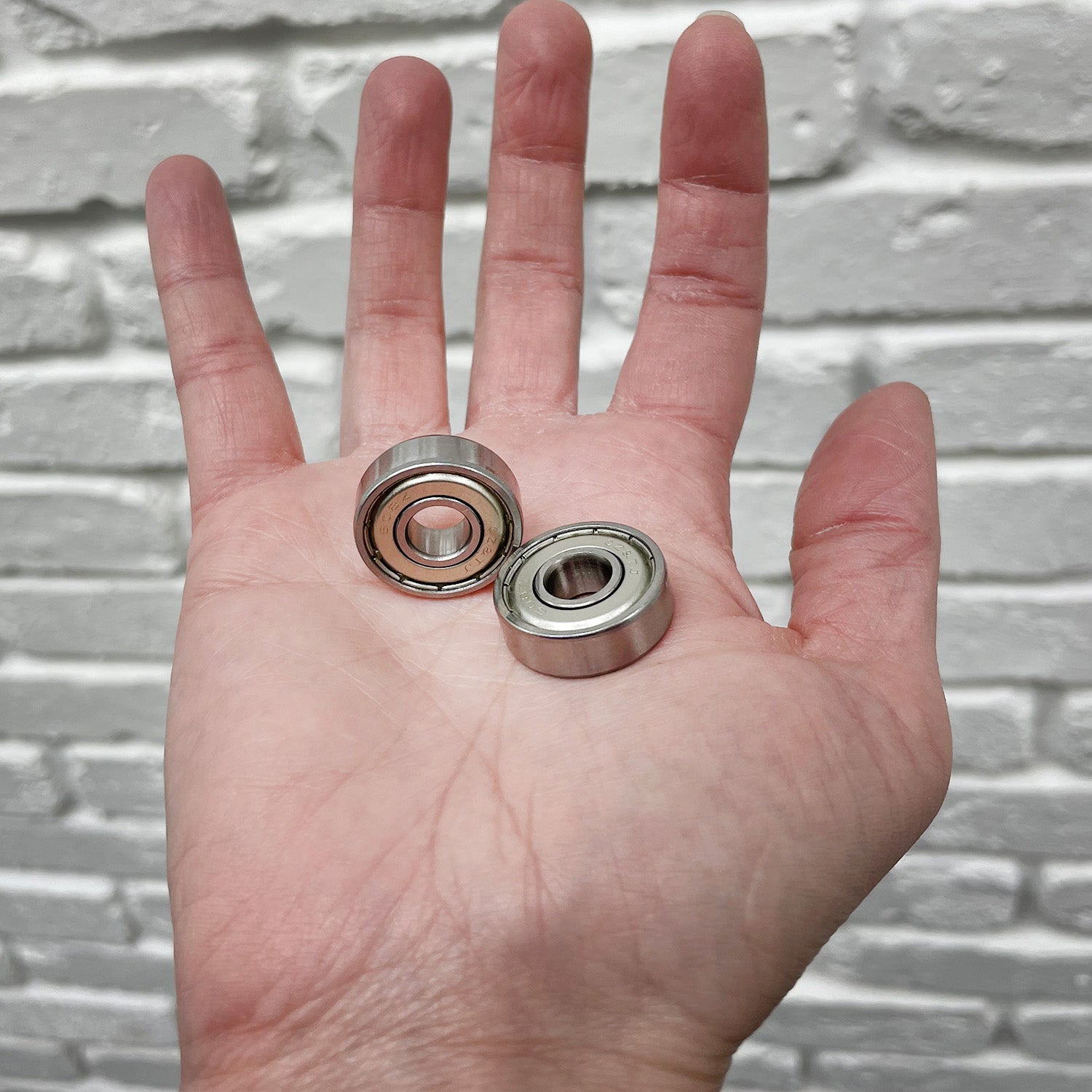 A hand holding two 608ZZ (608Z) ABEC-5 shielded scooter wheel bearings, showcasing their metal shields and compact design.
