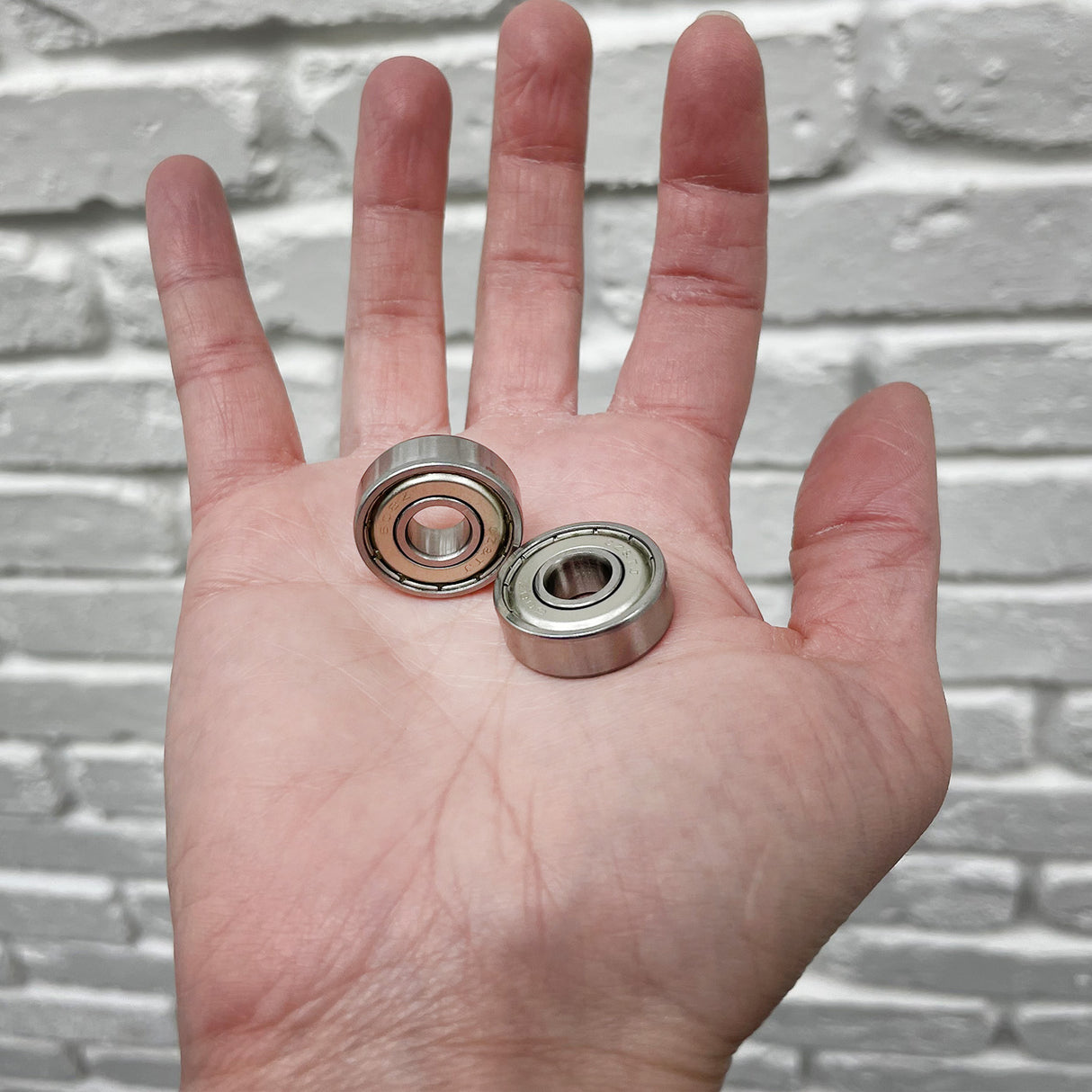 A hand holding two 608ZZ (608Z) ABEC-5 shielded scooter wheel bearings, showcasing their metal shields and compact design.