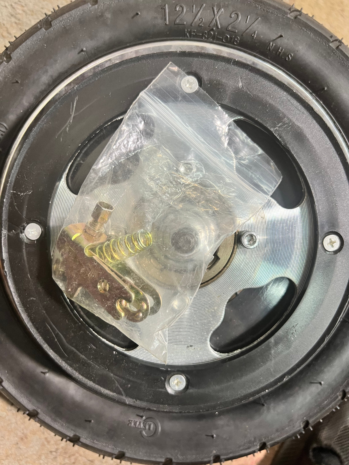 Rear Wheel Assembly with Wire Spoke Rim for the Razor Pocket Mod (Versions 13-30) (Blemished) showing wheel with plastic bag and metal spring on top, close-up of screws.