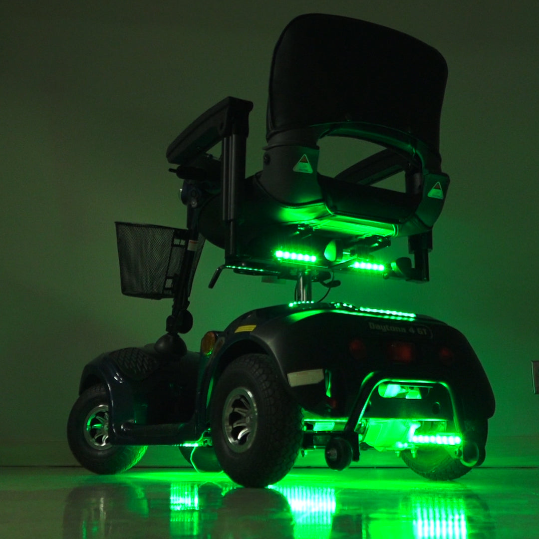 Multi-Color LED Light Kit for Mobility Scooters & Power Chairs, featuring green-lit strips on scooter wheels and a black mesh basket, enhancing both safety and visual appeal with various lighting modes.