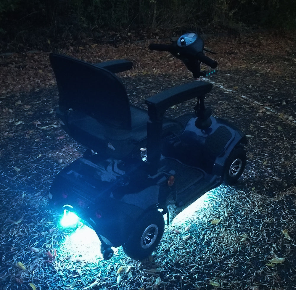 Multi-Color LED Light Kit for Pride Mobility Scooters, featuring a scooter with illuminated light strips and black handlebars. The kit includes multiple light functions, controlled via a hand-held remote.