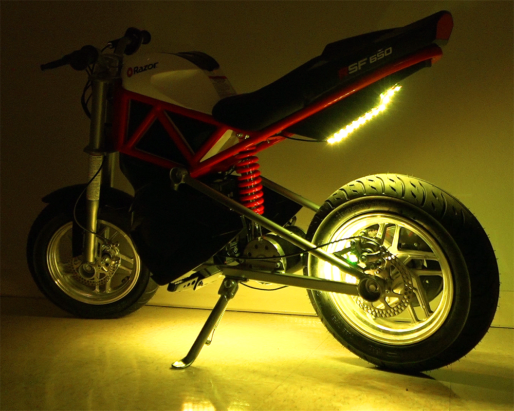 Multi-Color LED Light Kit for Razor Electric Bikes & Scooters featuring various light functions, visible attached light strips, and a close-up of the motorcycle wheel and kickstand showcasing the installation.