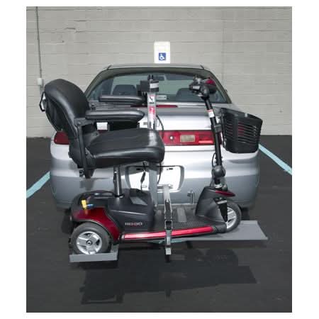 Pride Silver Star Power Tote Mini PT-150 Scooter Lift attached to a vehicle, showcasing its compact design for transporting smaller travel scooters and wheelchairs. Visible tire and part of the vehicle's rear.