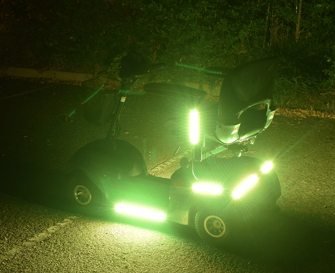 Multi-Color LED Light Kit for Pride Mobility Scooters installed on a scooter, showcasing bright, illuminated light strips on wheels and frame, highlighting the vibrant, customizable lighting options for enhanced visibility and style.