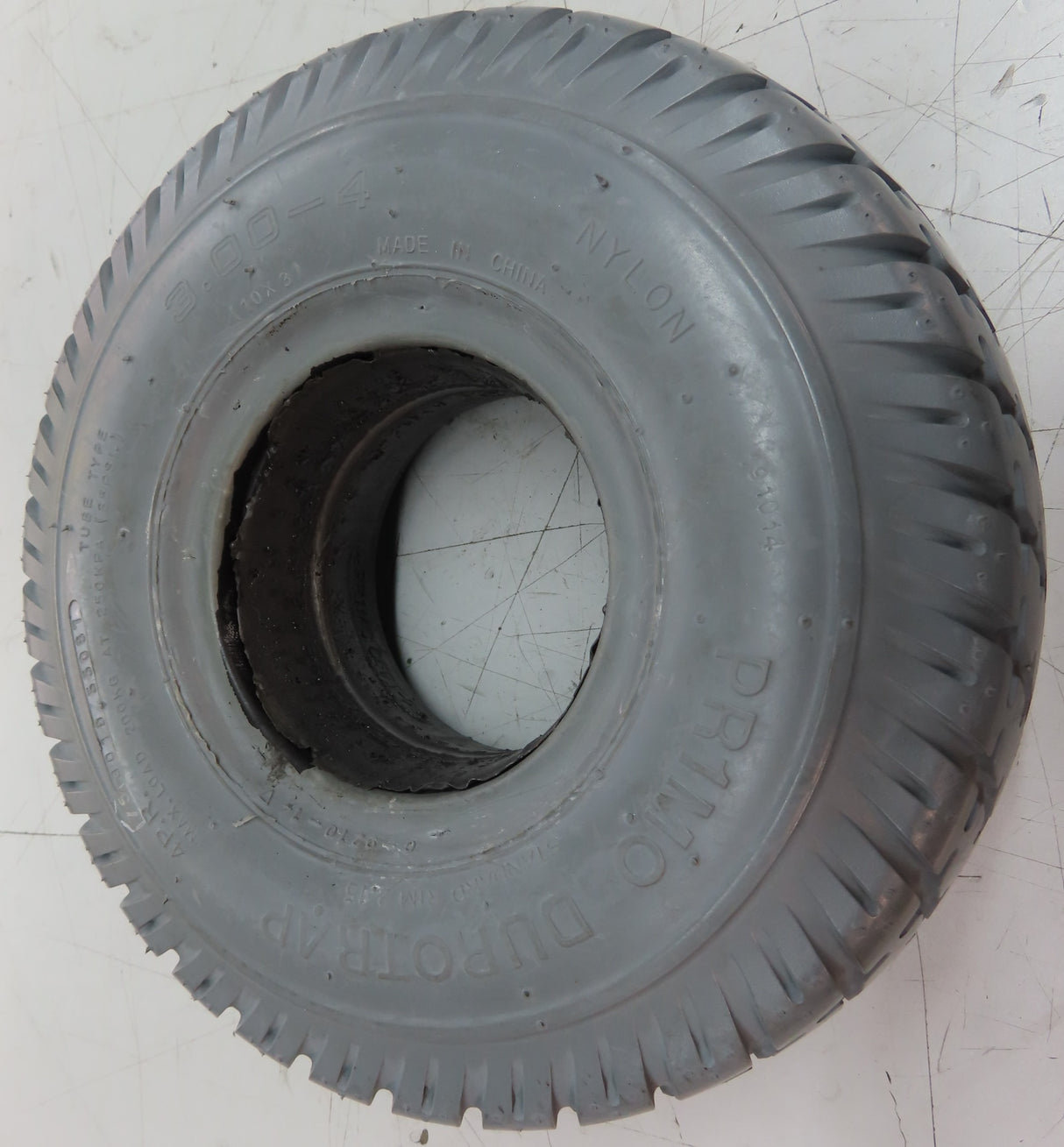 3.00-4 (10x3, 260X85) Foam-Filled Mobility Tire (2-5/8 Bead Width) with Durotrap C9210 Tread (Blemished), shown on a tile floor, featuring a central hole and non-marking gray surface.