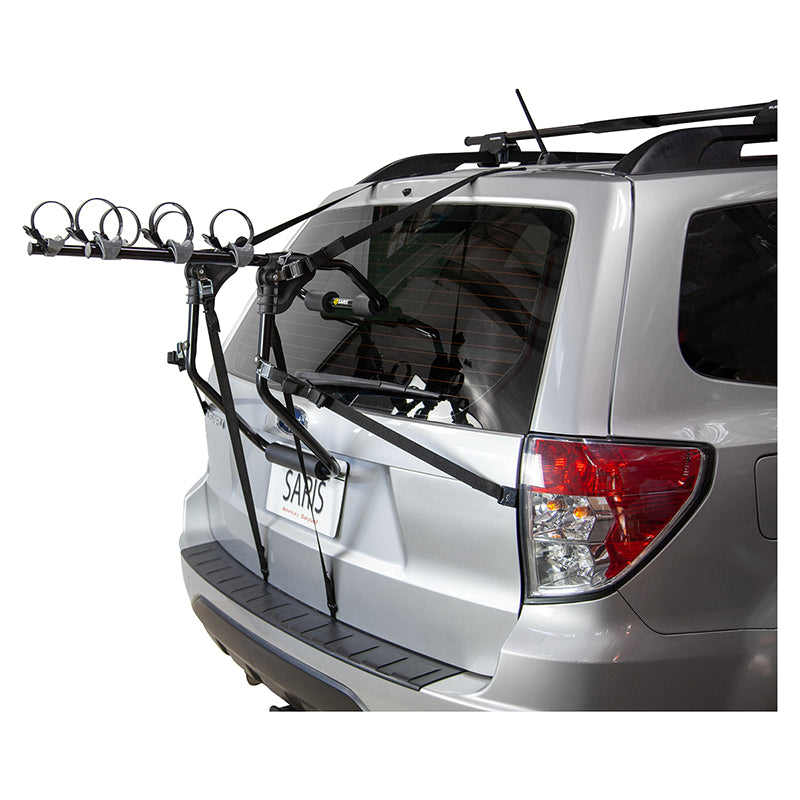 Guardian Trunk Rack attached to a car, featuring bike hold downs with ratcheting straps and spring-loaded buckles. The rack fits sedans, hatchbacks, and vans, with padded hooks protecting the vehicle's finish.