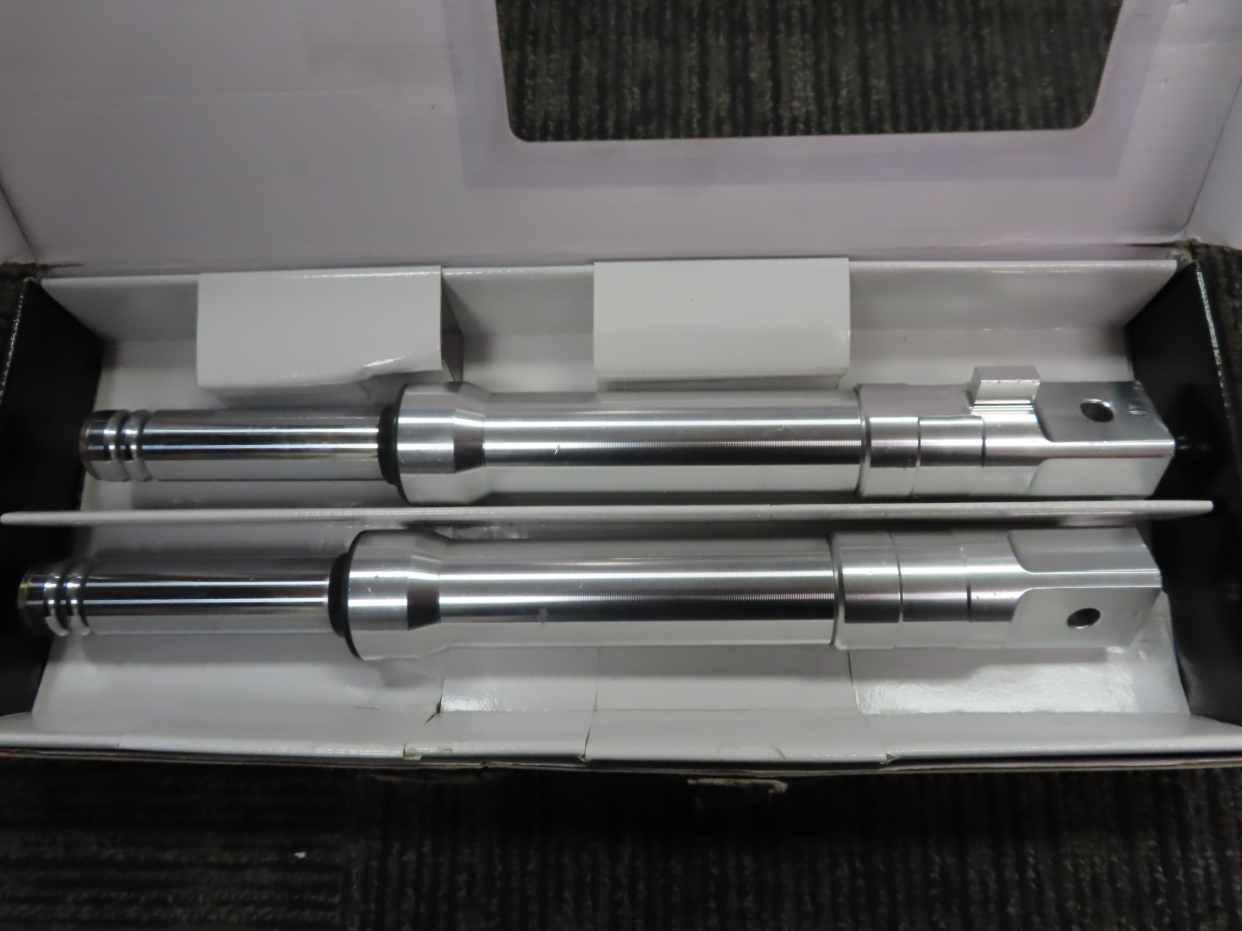 Silver Front Forks for the Honda Ruckus (NPS50) (Blemished) displayed within a box, showcasing two sturdy metal rods designed for drum-brake front wheels, highlighting NCY's high-performance accessory.