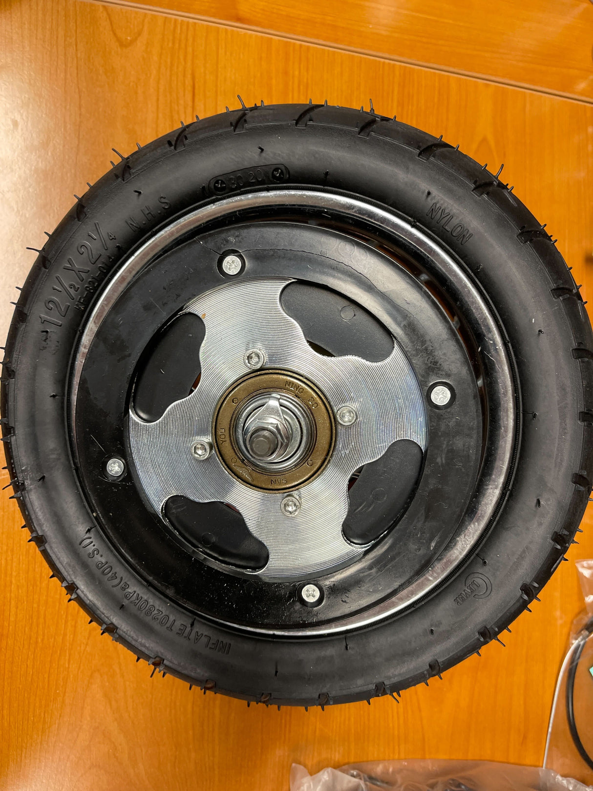 Rear Wheel Assembly with Wire Spoke Rim for the Razor Pocket Mod (Versions 31+) (Blemished) displayed on a wooden table, highlighting the tire, spokes, rim, and visible wheel bearings.