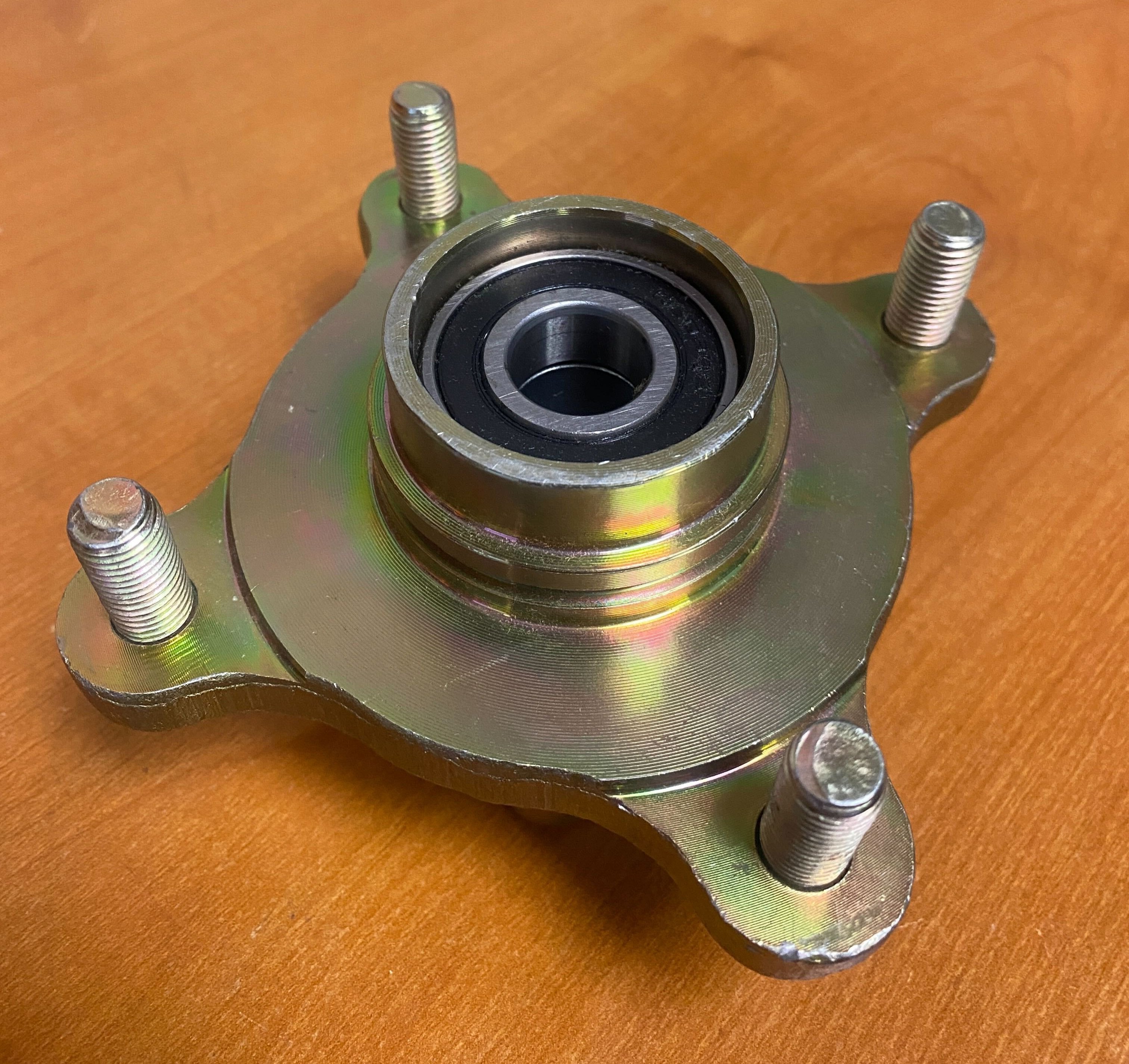 Front Wheel Hub for Hammerhead Off-Road® 150cc Go-Karts (Blemished): A metal wheel hub with bolts and a round center, designed for go-karts, shown on a wood surface.