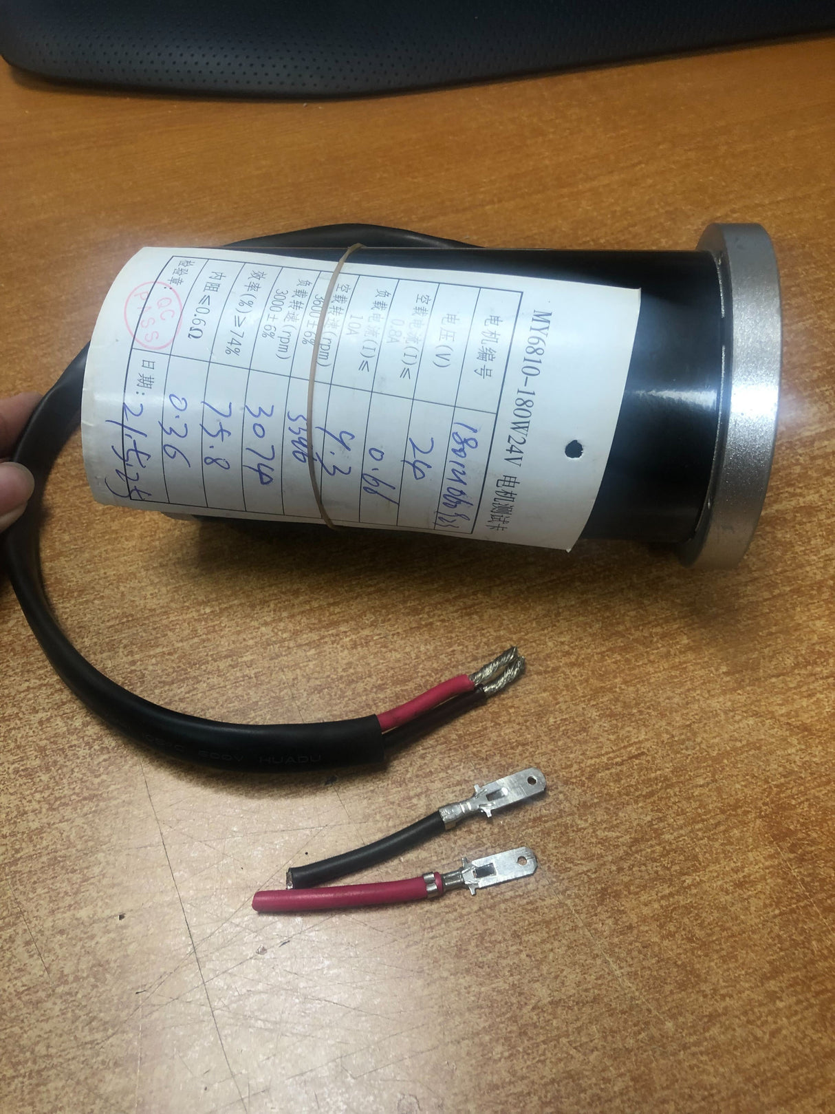 Hand holding piece of paper and wire on table, showcasing Drive Motor (MY6810) for Go-Go Elite Traveller (SC40E/SC44E) and Ultra X (SC40X/SC44X) Mobility Scooters (Blemished).