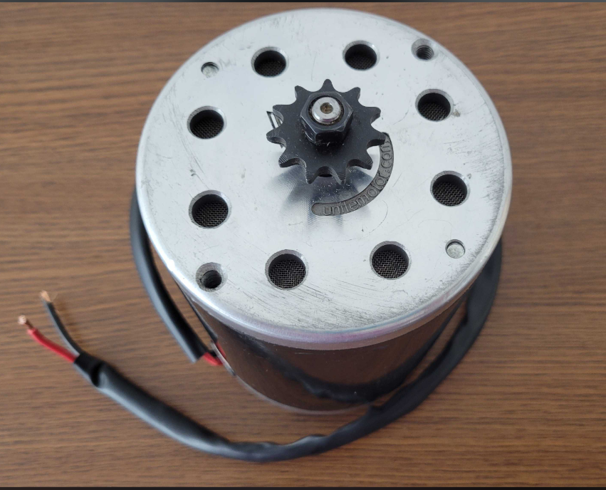 24 Volt 500 Watt MY1020 Electric Motor with 11 Tooth 8mm 05T Chain Sprocket (Blemished), showing a small metal device with a black wire, gear close-up, and multiple mounting holes on a white surface.