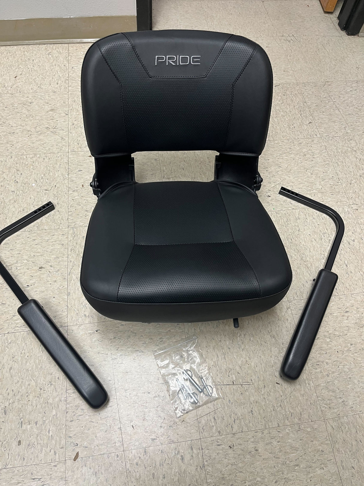 18 Black Vinyl Molded Seat Assembly for Pride Mobility Scooters featuring a padded seat, molded plastic back, and armrests, shown on a tile floor.