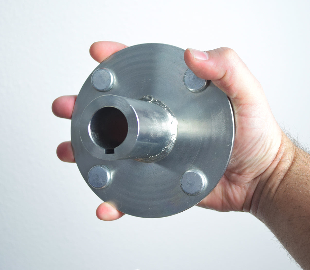 Hand holding the 4 x 4 Go-Kart Live Axle Hub with 1 to 3/4 Step-Down, showing the metal hub's four lug nuts and inner bore designed for a 1/4 axle key.