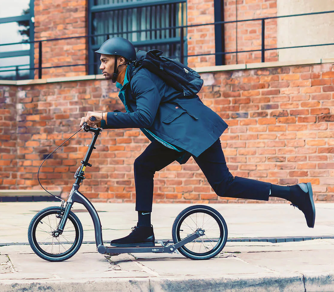 Man riding a scooter with the 12-1/2x2-1/4 (57-203/62-203) Kick Scooter Tire with Q203 Tread, showcasing its durable, pneumatic design and street tread for enhanced traction.