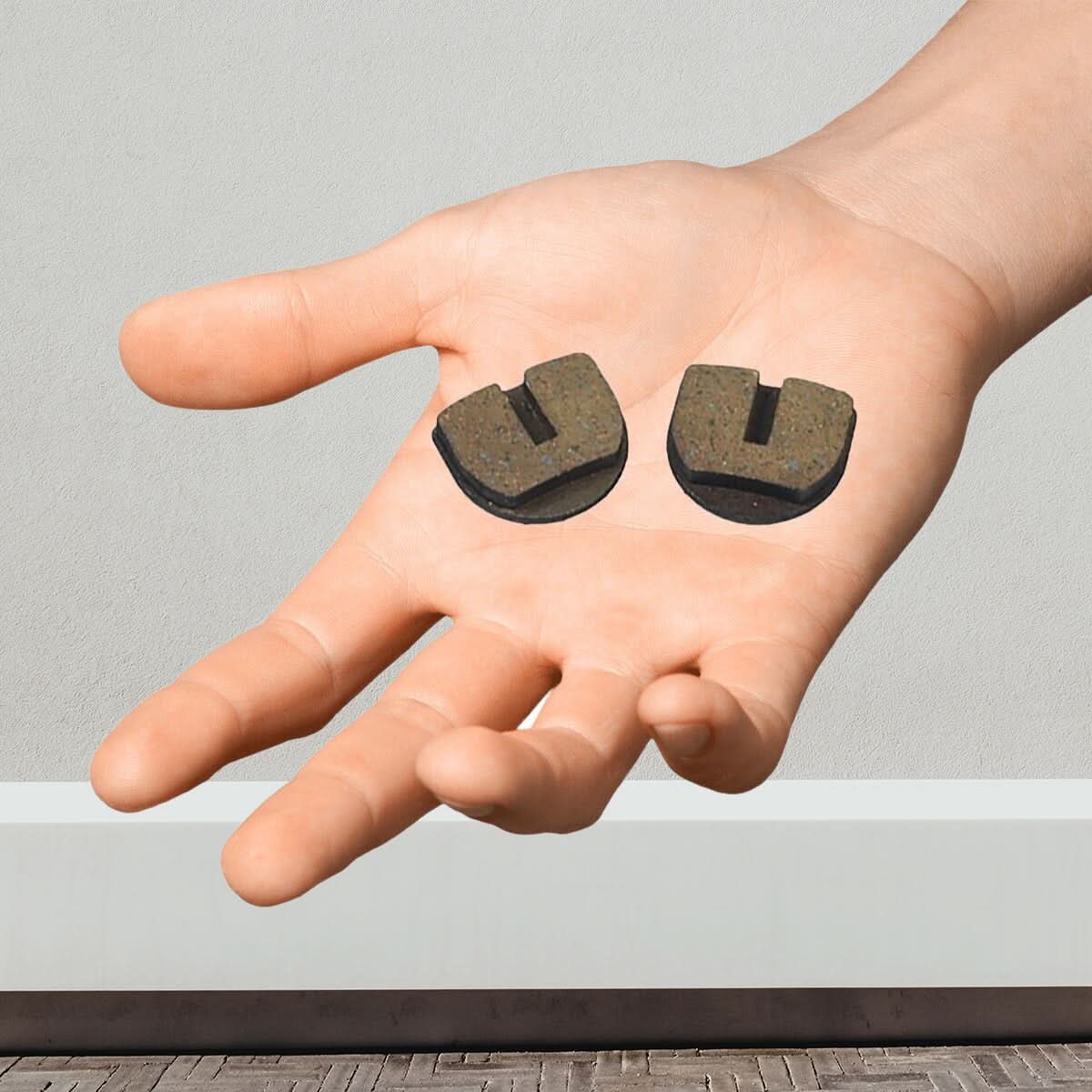 Hand holding a pair of Rounded Brake Pads for Standard & YK2 Flame Calipers (Set of 2), showcasing the sintered copper flecks embedded in the pads for enhanced durability and performance.