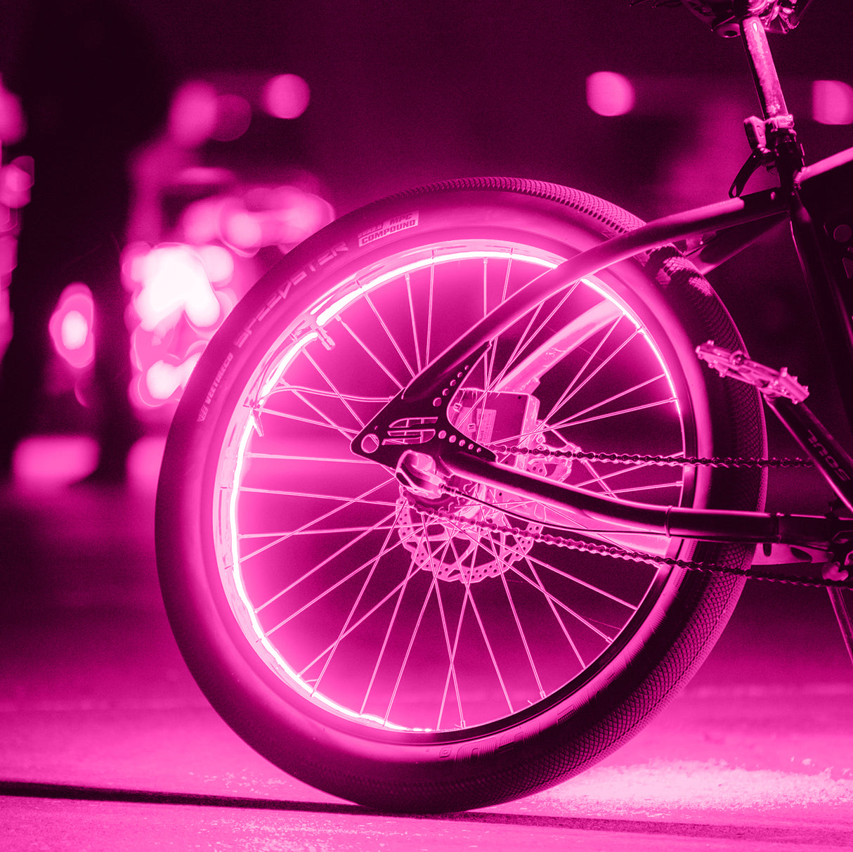 Close-up of a bicycle wheel with pink lights, showcasing the Firefly Valve Stem Light for Bikes & Scooters, a motion-activated LED light replacing the cap on the bike's inner tube valve.