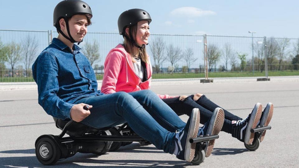 A man and woman ride a hoverboard go-kart, showcasing the 4 front caster with fork and axle, part of the Hoverboard Go-Kart Kit.