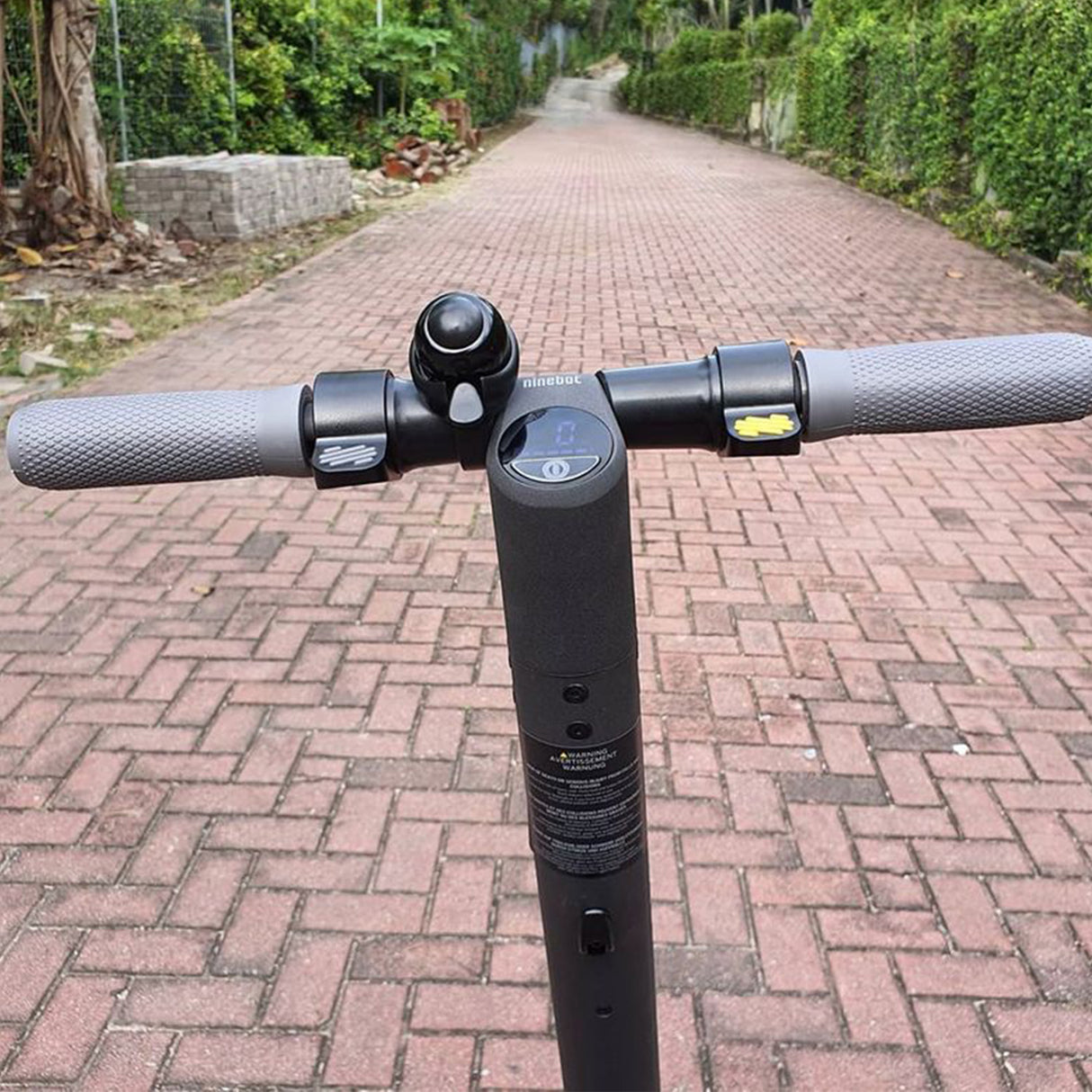 Universal Thumb Throttle for Electric Scooters on a brick path, showcasing its design and compatibility with various scooter models. The throttle fits standard 7/8 handlebars and uses a 3-pin Molex connector.