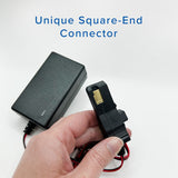 Hand holding a 12 Volt Battery Charger for Power Wheels Ride-On Toys, featuring a square-end connector and built-in charge indicator.