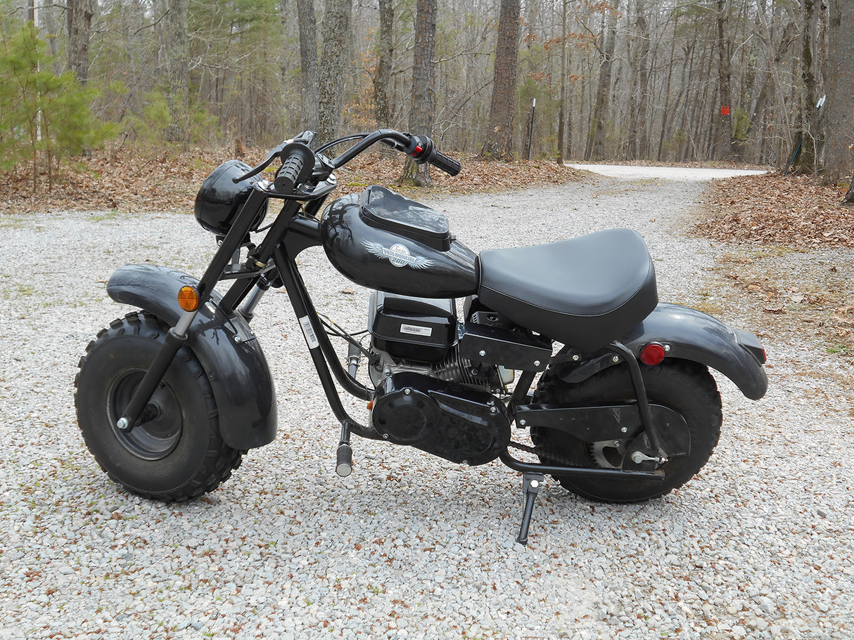 Black Left Brake Lever for the Baja Mini Bike MB165 & MB200, shown close-up on the motorcycle parked on gravel, highlighting its heavy-duty design and compatibility with Baja Heat, Mini Baja, and Baja Warrior models.