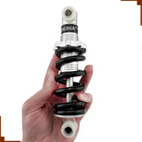 A hand holding a black and silver shock absorber for the Razor Dirt Quad ATV, showcasing its coil and detailed design.