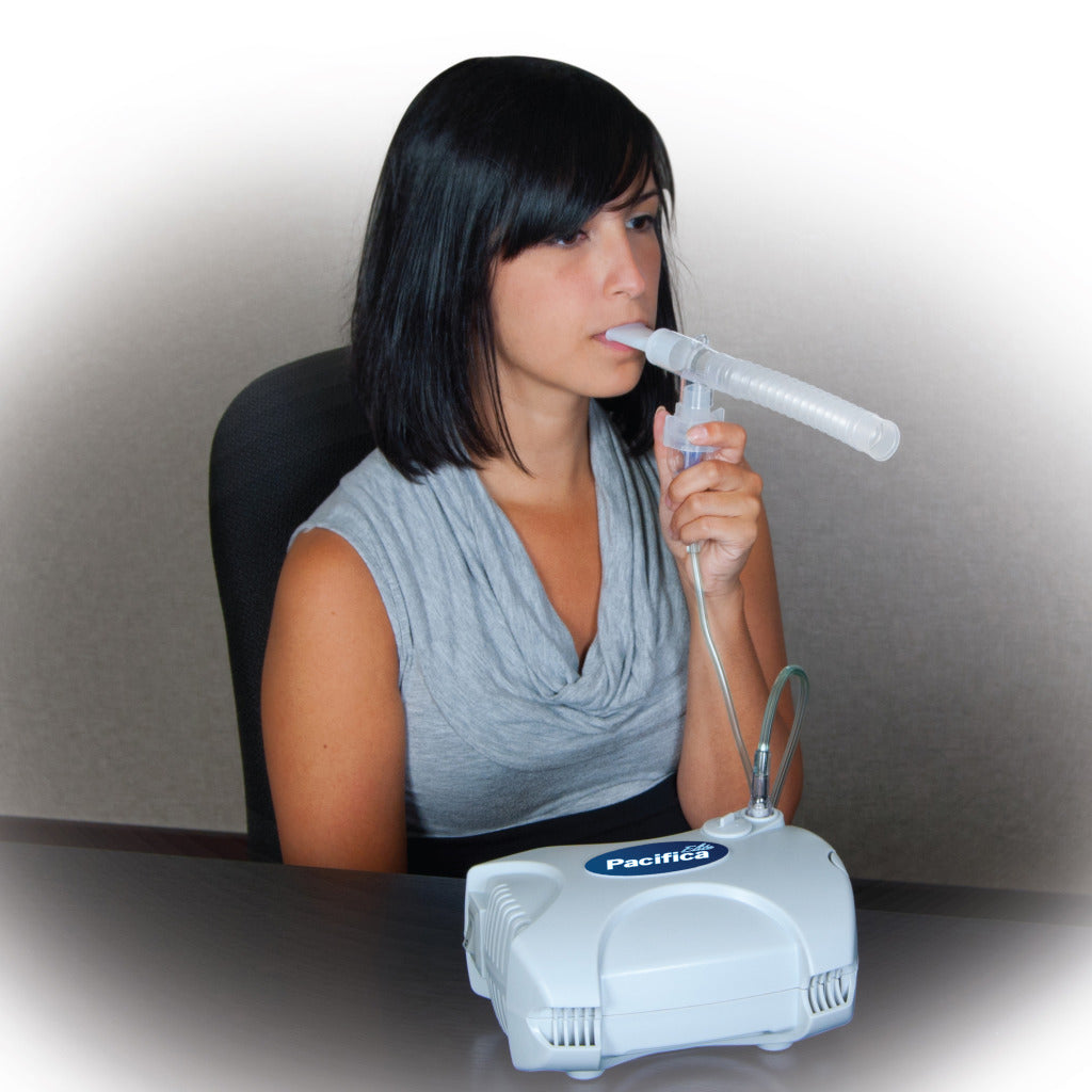 Woman using the Drive Medical Pacifica Elite Compressor Nebulizer, inhaling through a tube connected to a compact, white device designed for efficient and quiet respiratory treatment.