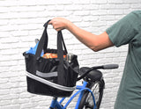 Lift Off Front Basket for Bikes & Scooters attached to a bicycle's handlebars, held by a person. The basket has a drawstring flap and is filled with various items, showcasing its storage capacity.