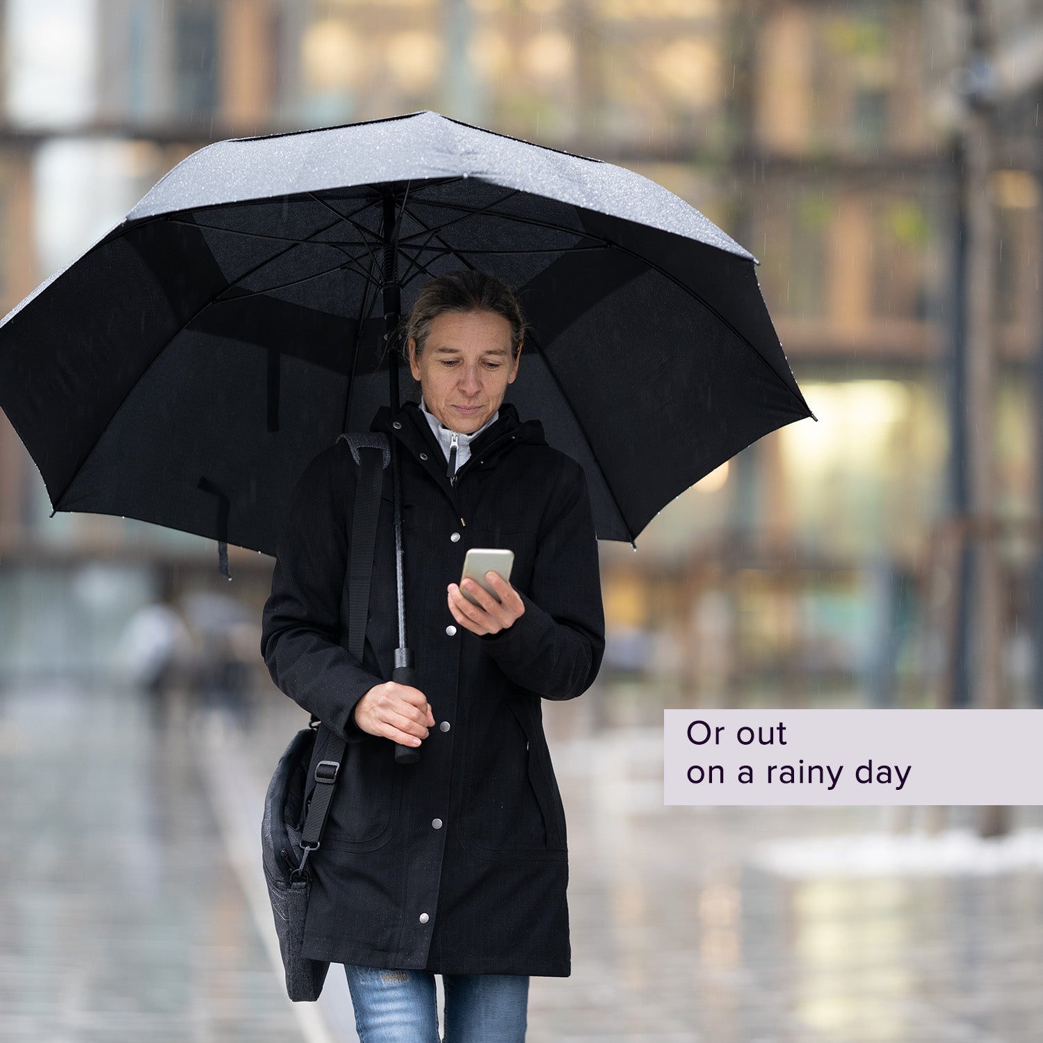 Man holding the Wind Resistant Vented Golf Umbrella, looking at his phone. The umbrella features eight vented panels and a soft foam hand grip, designed to withstand windy and rainy conditions.