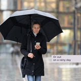 Man holding the Wind Resistant Vented Golf Umbrella, looking at his phone. The umbrella features eight vented panels and a soft foam hand grip, designed to withstand windy and rainy conditions.