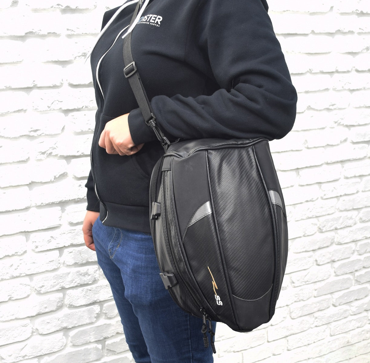 Person wearing a black jacket and blue jeans, holding a black Tail Bag for Electric Bikes. The bag features a sleek design with a sturdy build, ideal for carrying essentials.