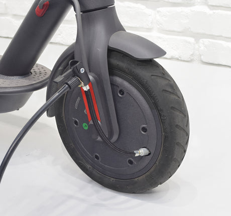 5” Black Rubber Inner Tube Valve Extender attached to a black wheel with a visible cable, showcasing its braided nylon cover and Schrader valve connectors on both ends.