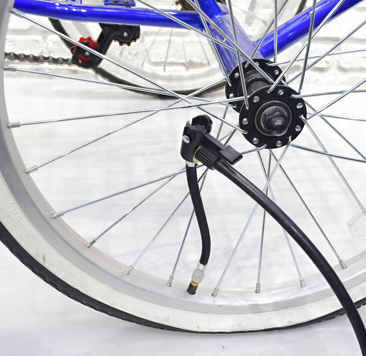 5” Black Rubber Inner Tube Valve Extender attached to a bicycle tire, with a pump nearby, showing the male Schrader valve connector and braided nylon protection.