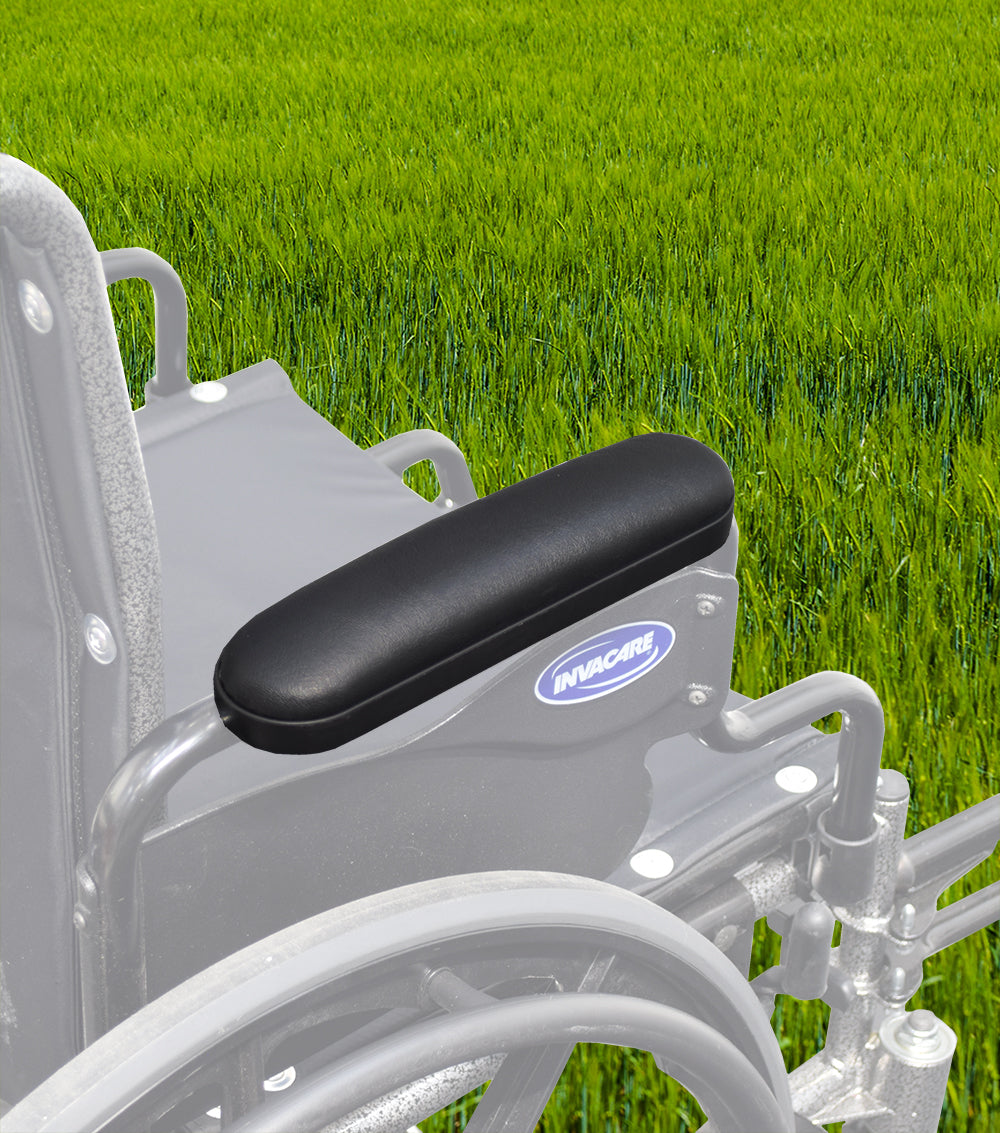 Black 10 Desk Length Padded Vinyl Armrest for Wheelchairs (Set of 2) shown in close-up on a wheelchair in a grassy field, highlighting the armrest's sleek design and mounting holes.