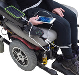 A person in a wheelchair holding a phone with an AlveyTech XLR Dual Port USB Charging Adapter with Digital Voltage Meter attached to the chair's battery charger port.