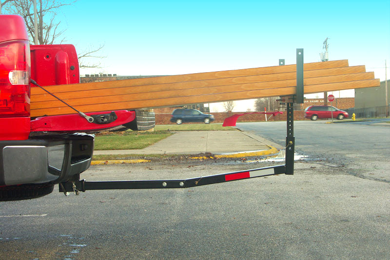 Hitch Mounted Bed Extender attached to the back of a red truck, providing extended support for long items. The road and sky are visible in the background.