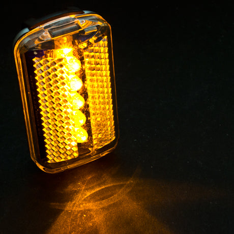 HL-L515 LED Headlight close-up, showcasing its amber light on a black surface. Ideal for scooters and bikes, this Sunlite accessory enhances night visibility.