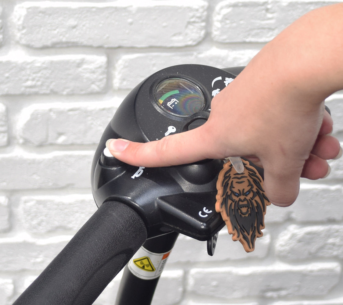 A hand holding the Horn Button Switch for the Go-Go Elite Traveller, Elite Traveller LR, Ultra X, & Pride Mobility Scooters, pressed onto a handlebar.