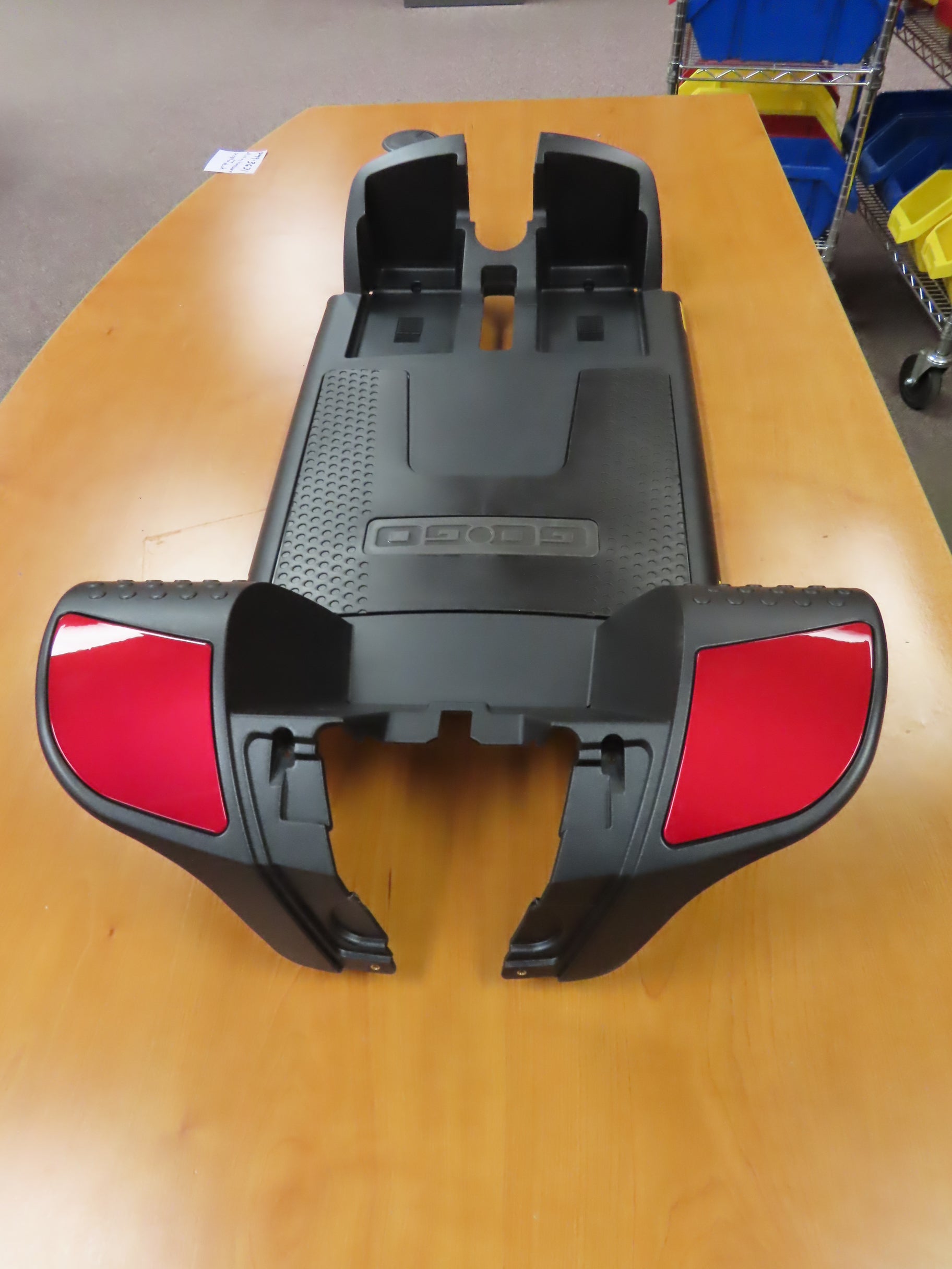 Front Shroud Assembly with Red Inserts for Go-Go Sport (S74) Models, showing a black and red plastic cover, missing fastening screws and with minor scratches, placed on a wooden table.