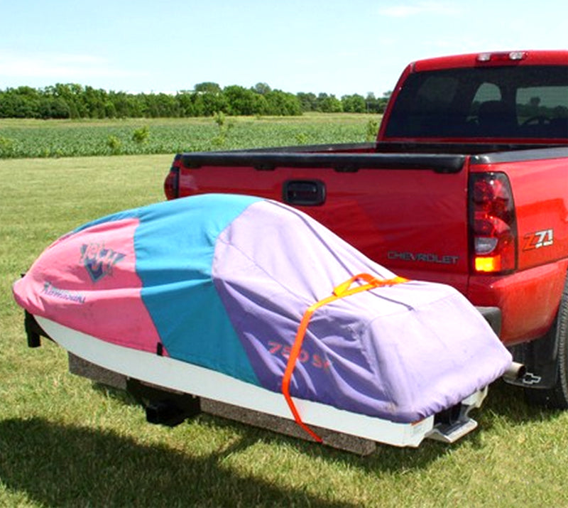 Jet Ski Carrier mounted on a red truck's hitch, showing twin rails and a ramp locked upright, with trees and sky in the background.