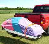 Jet Ski Carrier mounted on a red truck's hitch, showing twin rails and a ramp locked upright, with trees and sky in the background.