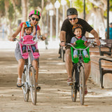 A family rides bicycles with two children in iBert Safe-T-Seat baby seats, positioned between the adult cyclist's arms and handlebars for a safe and enjoyable ride.