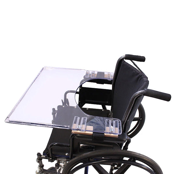 Mega Tray for Wheelchairs: a transparent polycarbonate tray attached to a black metal frame on a wheelchair, providing a stable surface for eating or writing.