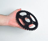 Hand holding the #40/41/420 Chain - 40 Tooth Rear Sprocket for Mini Bikes, showcasing the black gear with a center hole and four mounting holes.