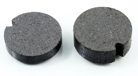 Close-up of two round black organic brake pads for Arctic Cat snowmobiles (1987-2006), featuring circular designs with central holes, one appearing slightly damaged.