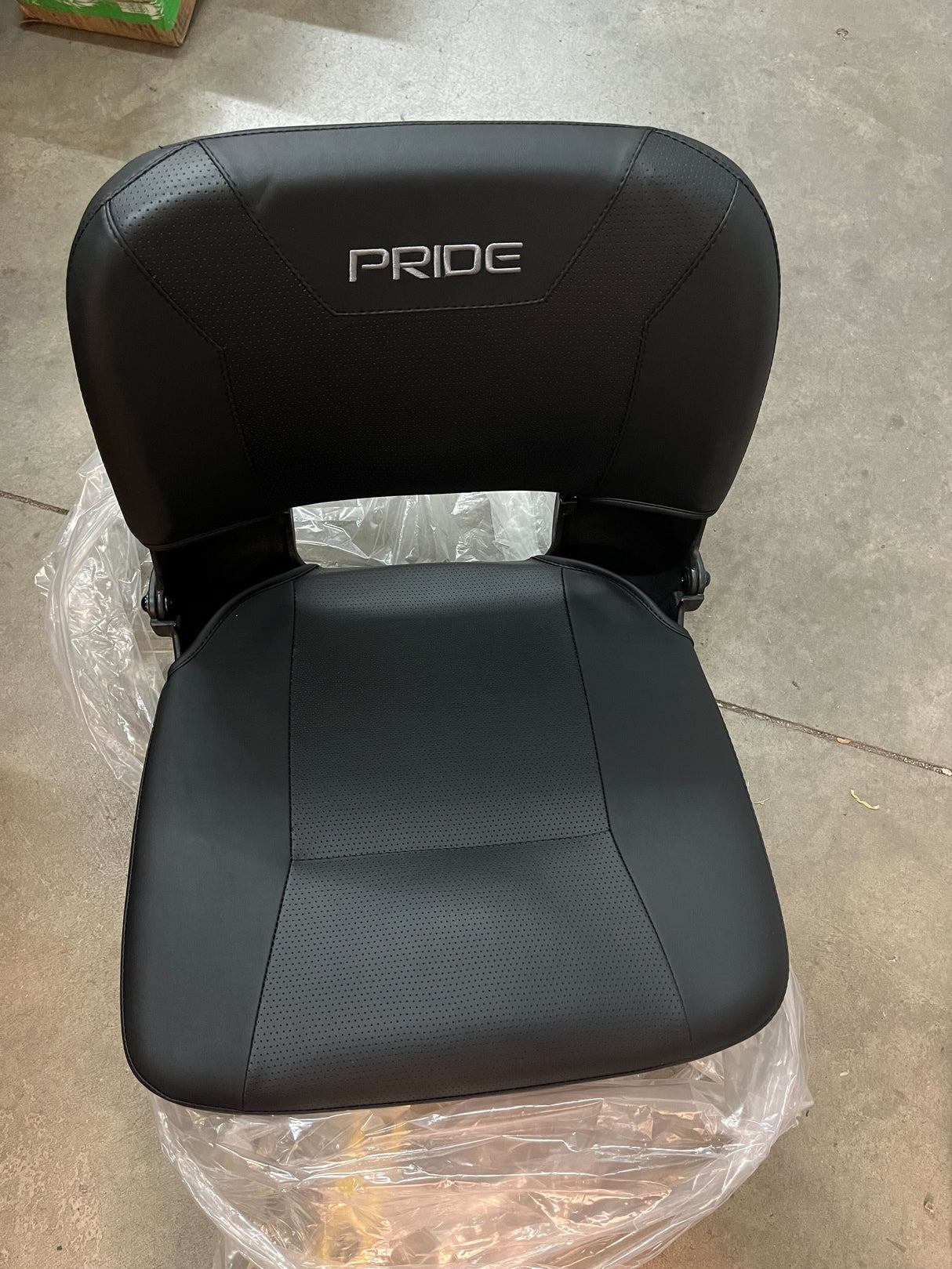 18 Black Vinyl Molded Seat Assembly for Pride Mobility Scooters (Blemished) wrapped in plastic, showcasing the black vinyl seat base with holes, seat back, and armrests.