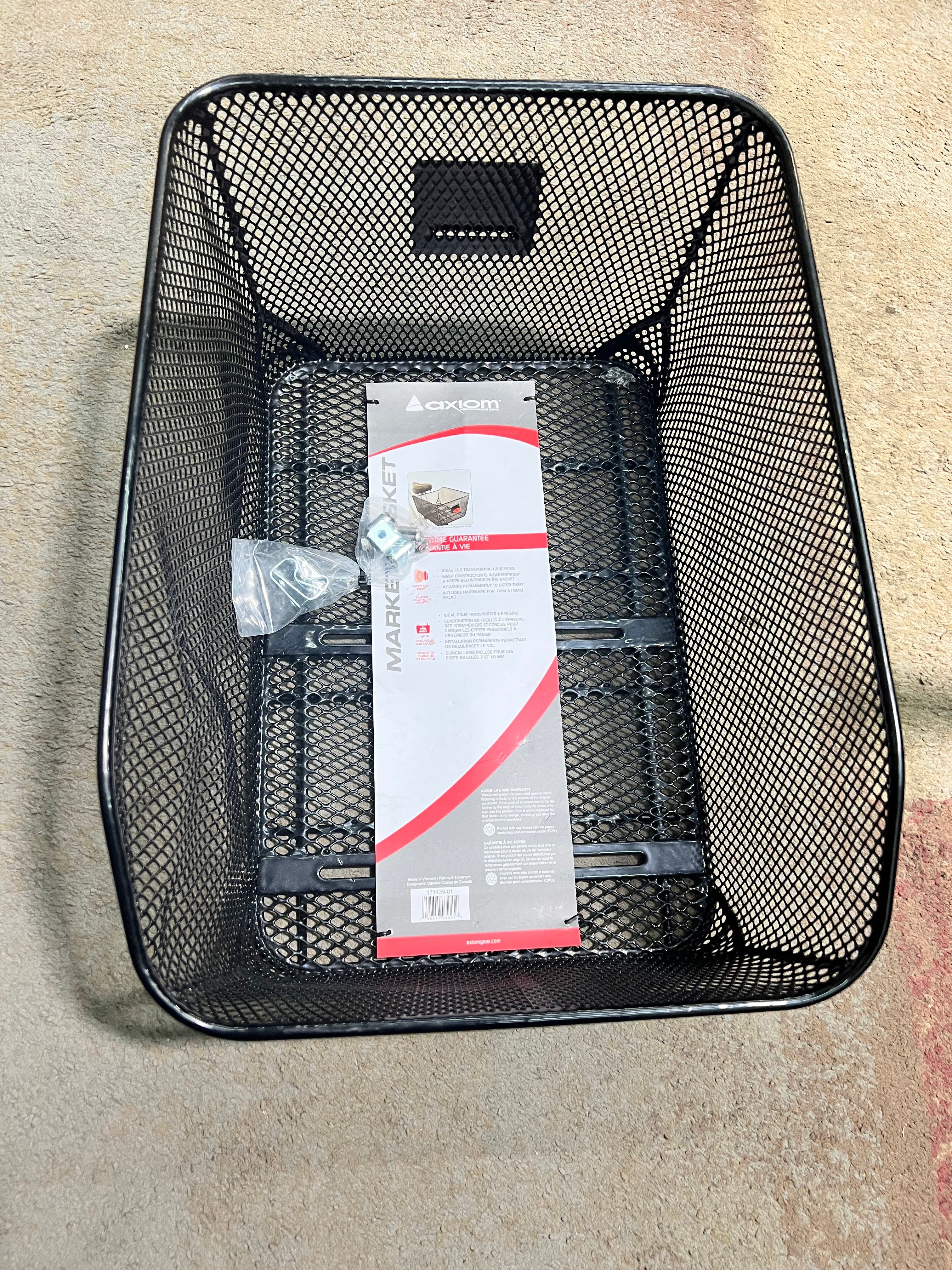 Market-Style Rear Basket for Bicycles (Axiom) (Blemished): A black, vinyl-dipped steel wire mesh basket mounted on a bike's rear rack, containing a red and white package.