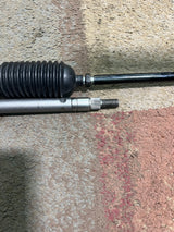 Steering Gear Assembly for the Coleman KT196 196cc 6.5 Hp Go-Kart (Blemished) featuring a close-up of metal components, including a steering shaft, tie rods, and a steering gearbox on a grey surface.