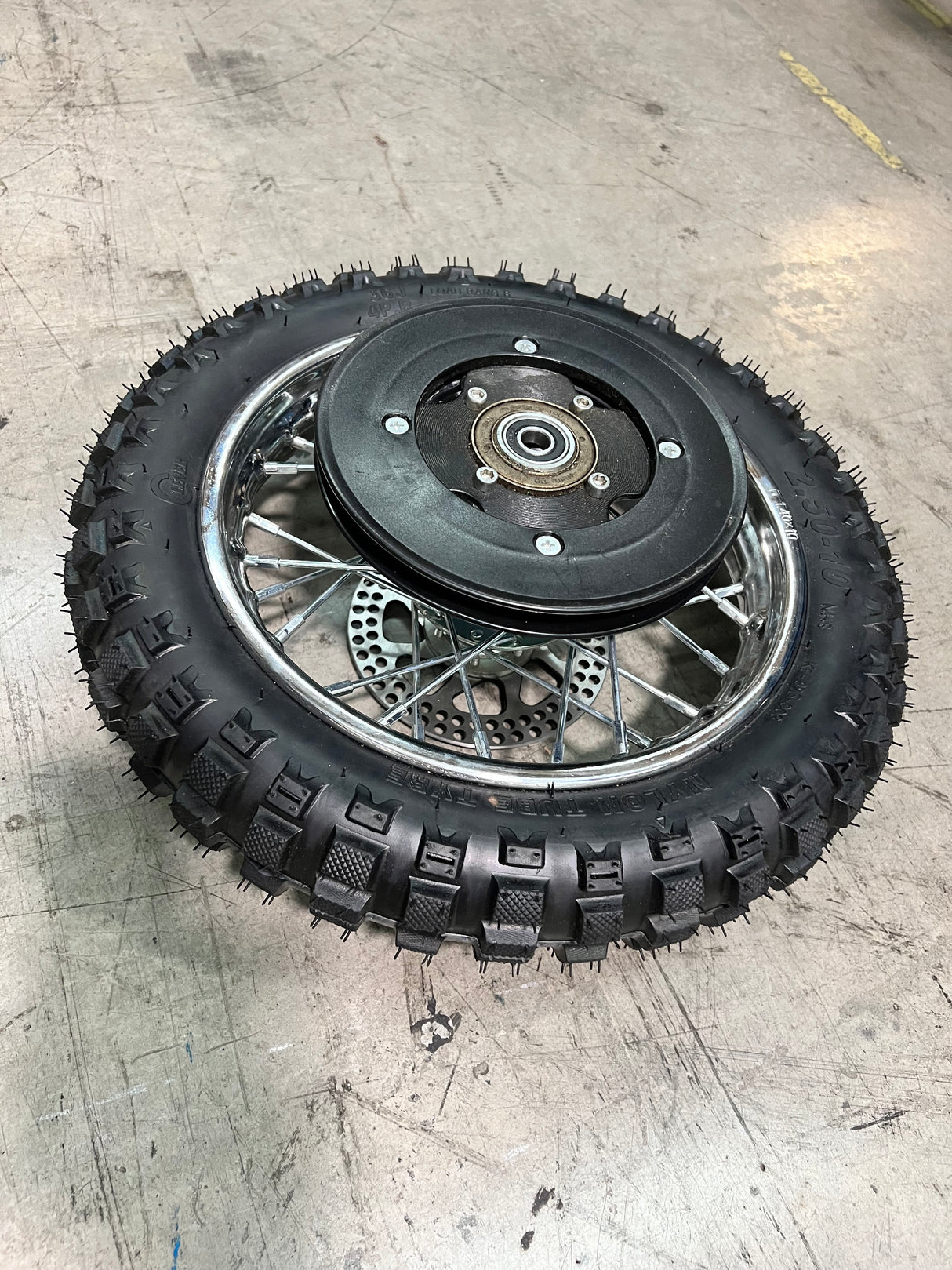 Rear Wheel Assembly for Razor MX500 and MX650 (Missing Hardware) featuring a black tire with a metal center, visible sprocket, and brake rotor, mounted on a rim.