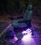 Multi-Color LED Light Kit for Jazzy Power Chairs shown on a wheelchair, featuring glowing light strips, suitable for outdoor use on grassy terrain.