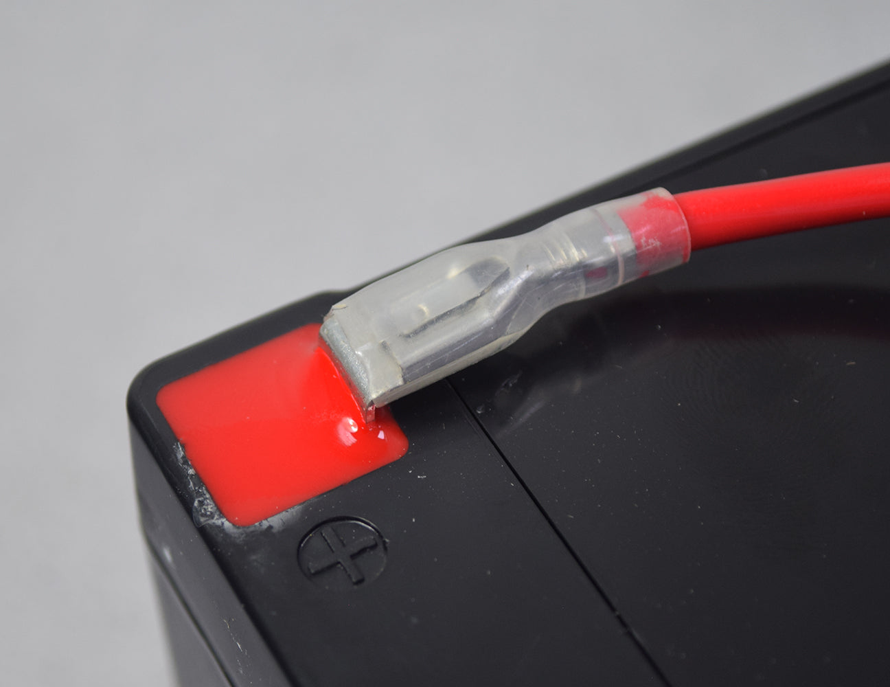 In-line 30 Amp ATM Blade Fuse Holder with Wire & 1/4 Battery Terminal Connectors, featuring a close-up of the red cable plugged into a black battery.